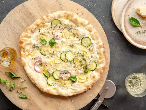 Pyszna pizza bianca z cukinią, cebulą i cytryną, posypana parmezanem i ziołami. Idealna na letni wieczór.