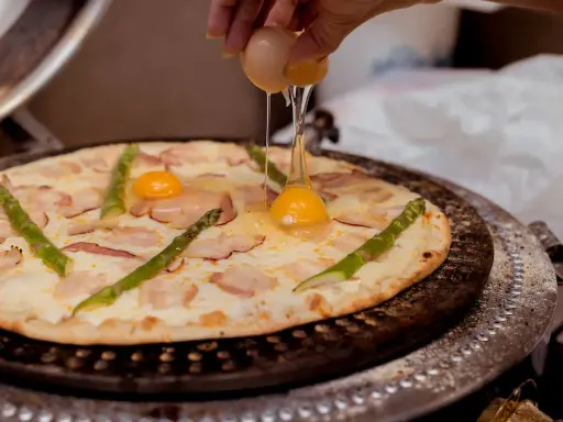 Kucharz dodaje jajko do pizzy z boczkiem i szparagami. Pyszna pizza z jajkiem w przygotowaniu.