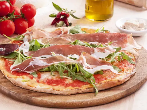 Pyszna pizza prosciutto z rukolą, pomidorami i oliwą z oliwek. Idealna na włoską ucztę.