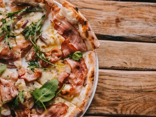 Pyszna pizza carbonara z chrupiącym boczkiem, rukolą i cebulą na drewnianym stole.