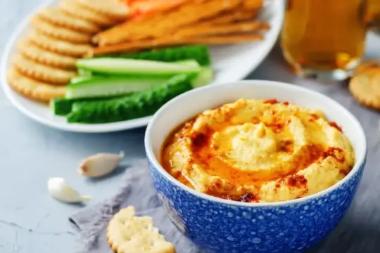 Pyszny, kremowy hummus, idealny jako sos do frytek, podany z chrupiącymi krakersami i świeżymi warzywami.