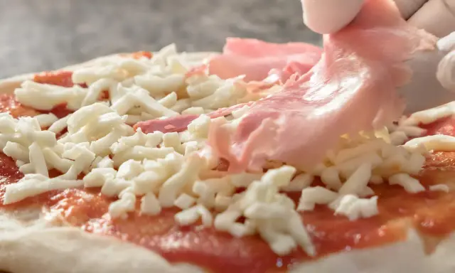 Rękawiczki zakładają cienkie plastry szynki parmeńskiej na pizzę z serem i sosem pomidorowym.