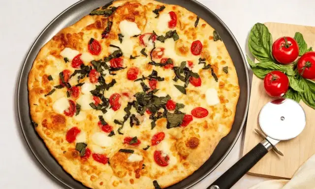 Pyszna pizza z serka wiejskiego, pomidorkami koktajlowymi i bazylią. Obok leży nóż do pizzy i świeże pomidory.