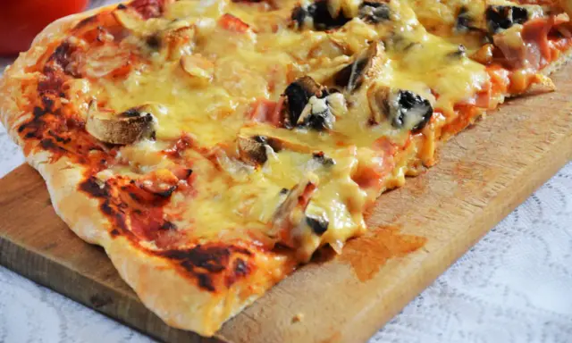 Pyszna pizza capriciosa z pieczarkami i szynką, roztopiony ser ciągnie się na chrupiącym cieście.