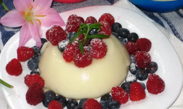 Panna cotta z malinami i borówkami, posypana cukrem pudrem. Idealny deser, który można zrobić według prostego legumina przepisu.
