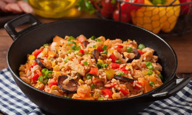 Pyszne jambalaya z kurczakiem, kiełbasą, kukurydzą i papryką w czarnej patelni.