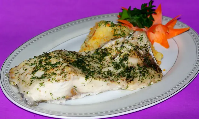 Pieczony amur z koperkiem i puree ziemniaczanym, ozdobiony marchewką i natką pietruszki.