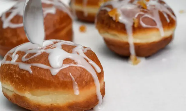 Lukier przepis na pączki. Łyżka polewa słodką masą pączki, które zaraz trafią na stół.
