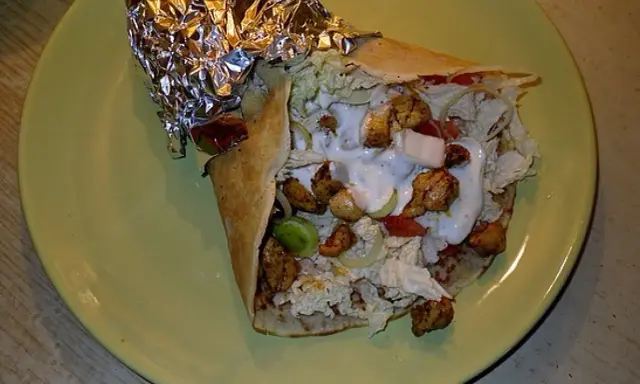 Pyszny kebab w tortilli z kurczakiem, warzywami i sosem na zielonym talerzu.