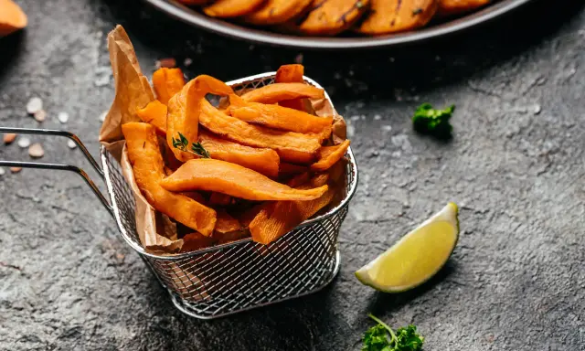 Chrupiące frytki z batatów z frytkownicy airfryer, podane w metalowym koszyku, z limonką i natką pietruszki.