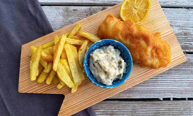 Chrupiące fish and chips z cytryną i sosem tatarskim na drewnianej desce.