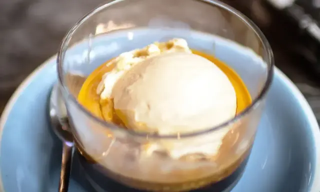 Pyszne affogato: gałka lodów waniliowych w gorącym espresso, podana w szklance na niebieskim talerzyku.