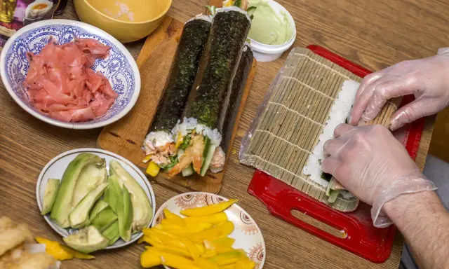 Przygotowanie uramaki: ryż, awokado, mango, krewetki i marynowany imbir czekają na zwinięcie w pyszne rolki sushi.