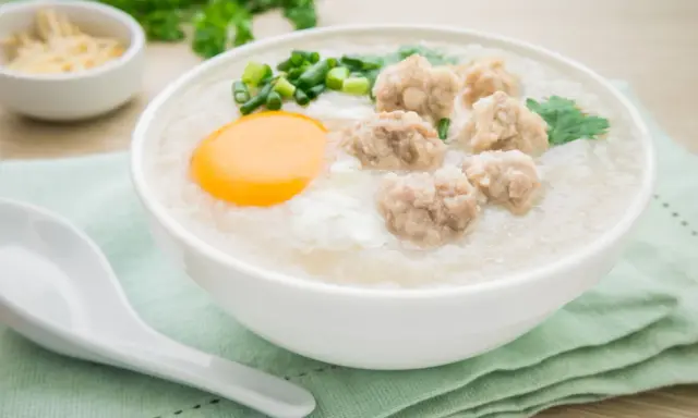 Miseczka aromatycznego congee z mięsnymi klopsikami, jajkiem i szczypiorkiem.