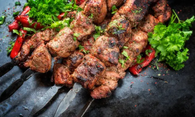 Soczyste kawałki mięsa na szpadach, przypominające kofta kebab, podane z pieczoną papryką i świeżą natką pietruszki.