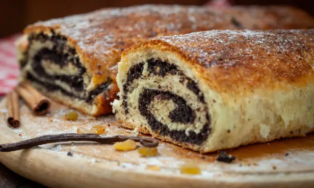 Pyszny makowiec który zawsze się udaje, z bogatym nadzieniem makowym, posypany cukrem pudrem. Obok laski wanilii i cynamonu.