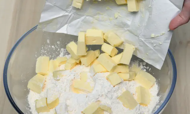 Kawałki zimnego masła dodawane do mąki w misce, kluczowy krok w sprawdzonym przepisie na kruche ciasto.