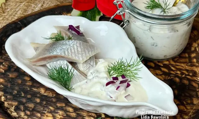 Matiasy w śmietanie z cebulą i ogórkiem, udekorowane koperkiem, prezentują się apetycznie.