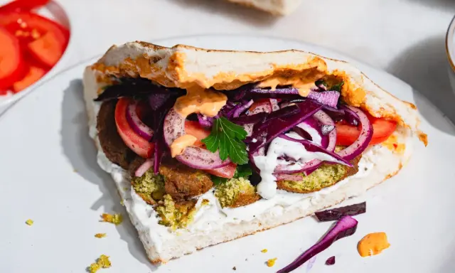 Pyszny falafel kebab w bułce z pomidorami, czerwoną cebulą, kapustą i sosami.