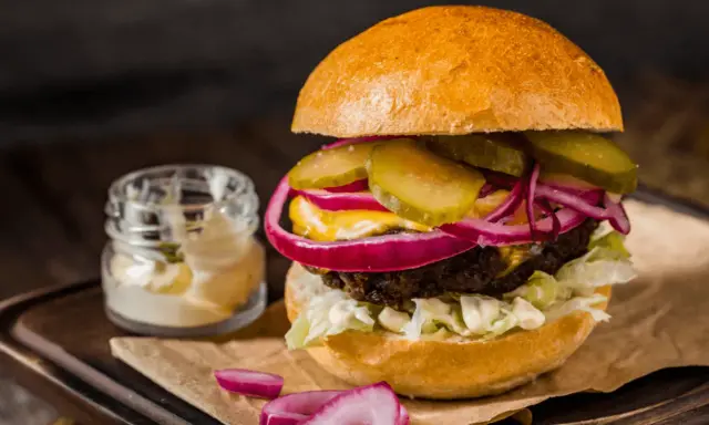 Soczysty burger z ogórkiem, czerwoną cebulą i majonezem, idealny do przygotowania, jak smażyć burgera na patelni.