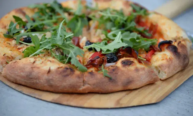 Idealne ciasto na pizzę z rukolą, oliwkami i papryką, wypieczone na drewnianej desce.
