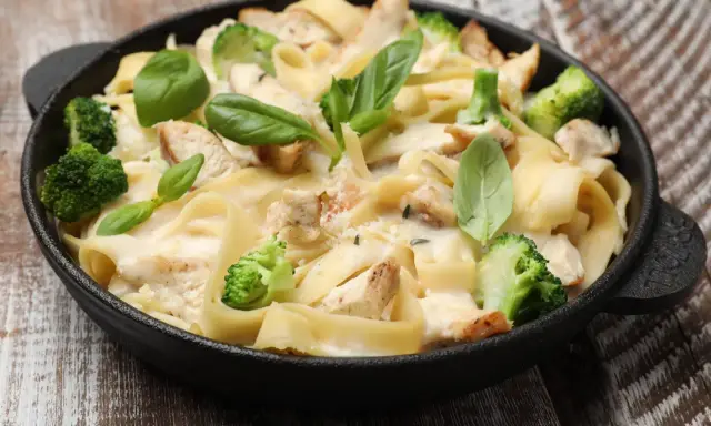 Tradycyjna potrawka z kurczaka z makaronem tagliatelle, brokułami i kremowym sosem, udekorowana świeżą bazylią.