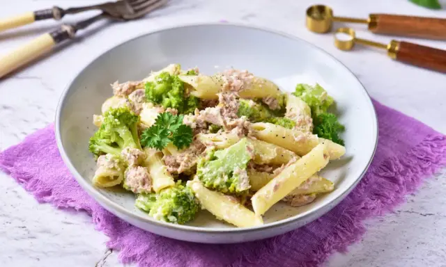 Penne z tuńczykiem i brokułami w kremowym sosie śmietanowo-serowym, udekorowane natką pietruszki.