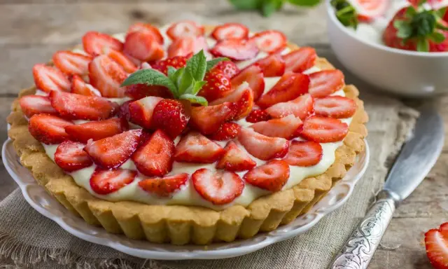 Pyszna tarta z truskawkami i kremem, ozdobiona listkami mięty. Idealna na letnie popołudnie.