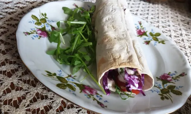 Pyszny lawasz kebab z czerwoną kapustą, pomidorem i rukolą na ozdobnym talerzu.