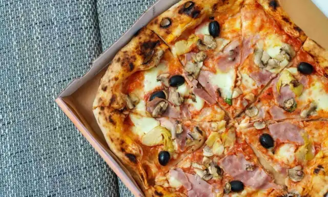 Pizza capricciosa z szynką, pieczarkami, karczochami i czarnymi oliwkami, w pudełku.