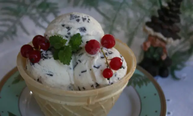 Lody straciatella w wafelku, ozdobione listkami mięty i czerwonymi porzeczkami.
