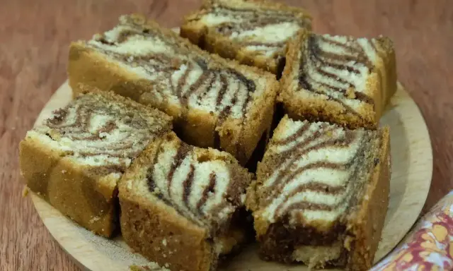 Puszyste ciasto zebra przepis. Pokrojone kawałki ciasta z charakterystycznym wzorem zebry ułożone na drewnianej desce.
