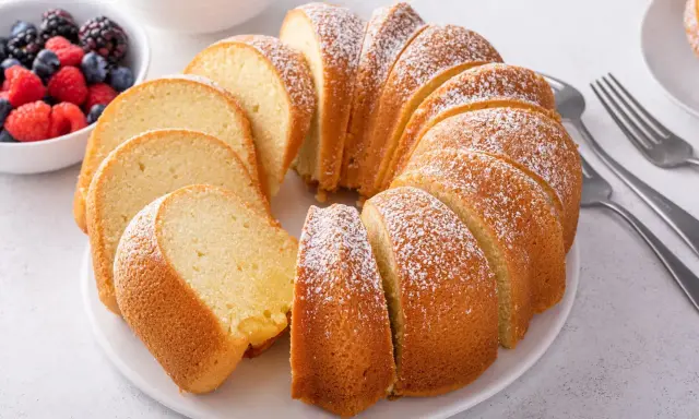 Puszysta, pokrojona wielkanocna babka posypana cukrem pudrem, obok miseczka z jagodami i malinami.