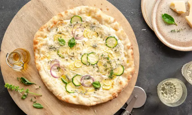 Pyszna pizza bianca z cukinią, cebulą i cytryną, posypana parmezanem i ziołami. Idealna na letni wieczór.