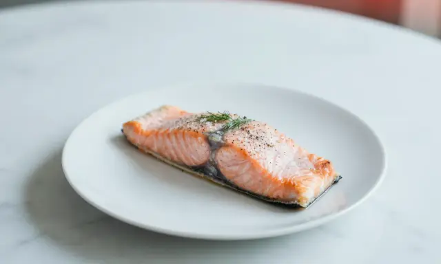 Soczysty łosoś z airfryer, doprawiony pieprzem i świeżym koperkiem, prezentuje się apetycznie na białym talerzu.