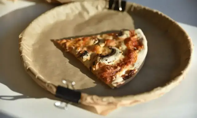 Kawałek pizzy z pieczarkami na papierowym talerzu. Zastanawiasz się, ile kalorii ma średnia pizza?