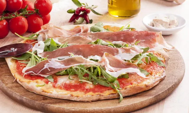 Pyszna pizza prosciutto z rukolą, pomidorami i oliwą z oliwek. Idealna na włoską ucztę.