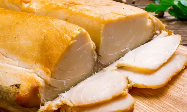 Dwa kawałki wędzonej ryby maślanej, jeden pokrojony w plastry, leżą na desce.
