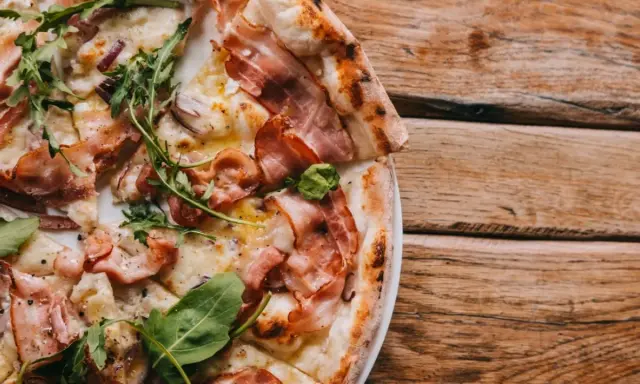 Pyszna pizza carbonara z chrupiącym boczkiem, rukolą i cebulą na drewnianym stole.