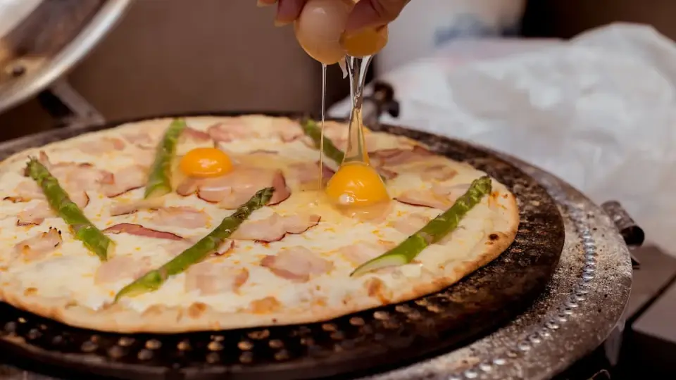 Kucharz dodaje jajko do pizzy z boczkiem i szparagami. Pyszna pizza z jajkiem w przygotowaniu.