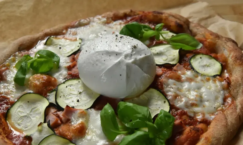 Pyszna pizza z burrata, cukinią i bazylią, posypana świeżo mielonym pieprzem.