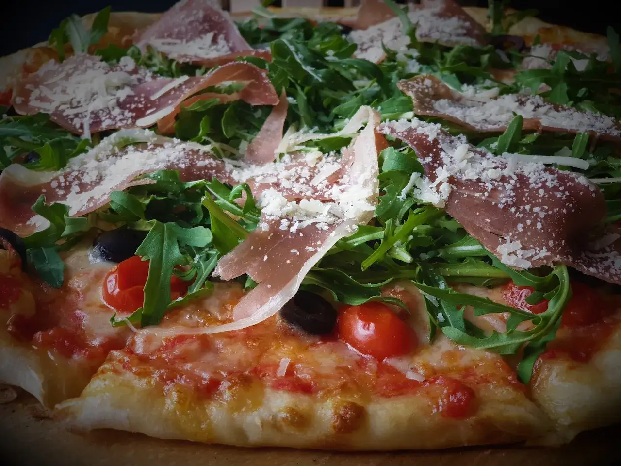 Pyszna pizza parma z rukolą, pomidorkami koktajlowymi, oliwkami i startym parmezanem.