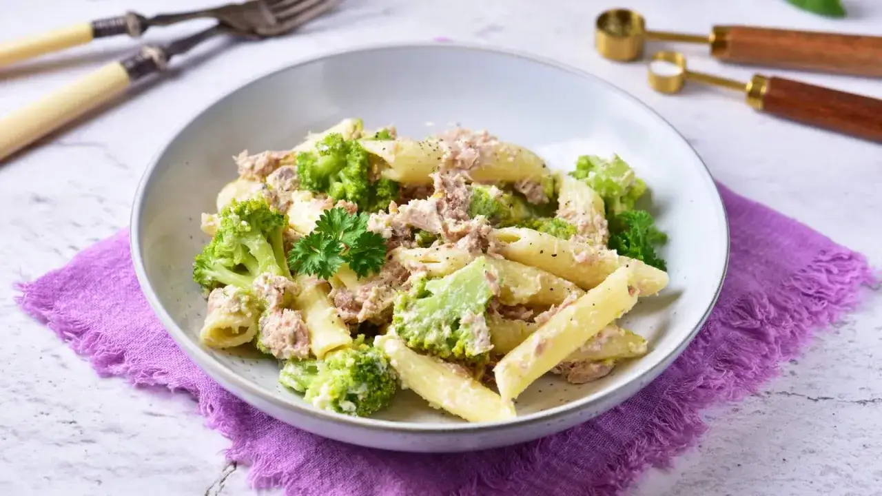 Penne z tuńczykiem i brokułami w kremowym sosie śmietanowo-serowym, udekorowane natką pietruszki.