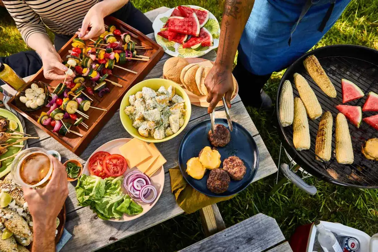 Pyszne jedzenie na grilla: szaszłyki warzywne, burgery, kukurydza, sałatka ziemniaczana i arbuz. Idealne menu na letnie spotkanie.