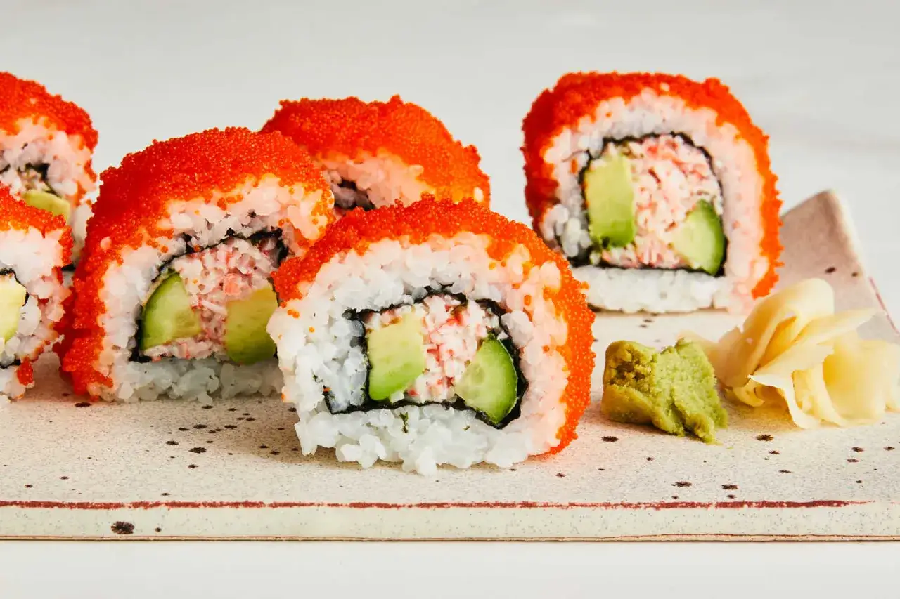 California sushi z krewetkami, awokado i ogórkiem, obtoczone w pomarańczowej ikrze. Obok wasabi i marynowany imbir.