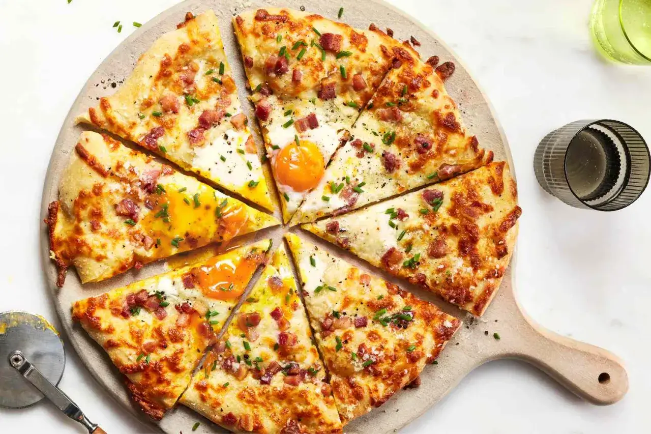 Pizza carbonara z jajkiem sadzonym i boczkiem, pokrojona na kawałki, prezentuje się apetycznie.