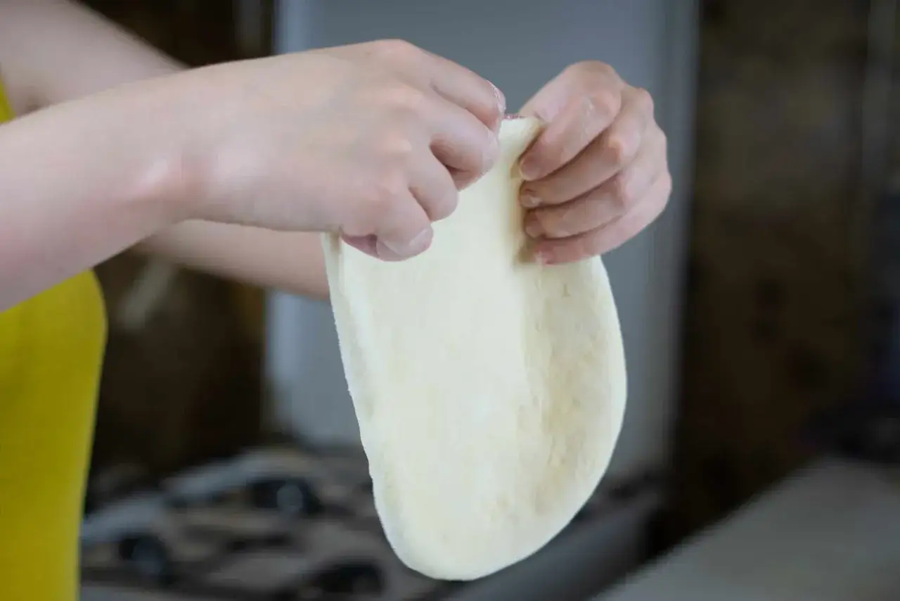 Dłonie formują elastyczne, białe ciasto, które zapowiada idealne ciasto na pizzę.