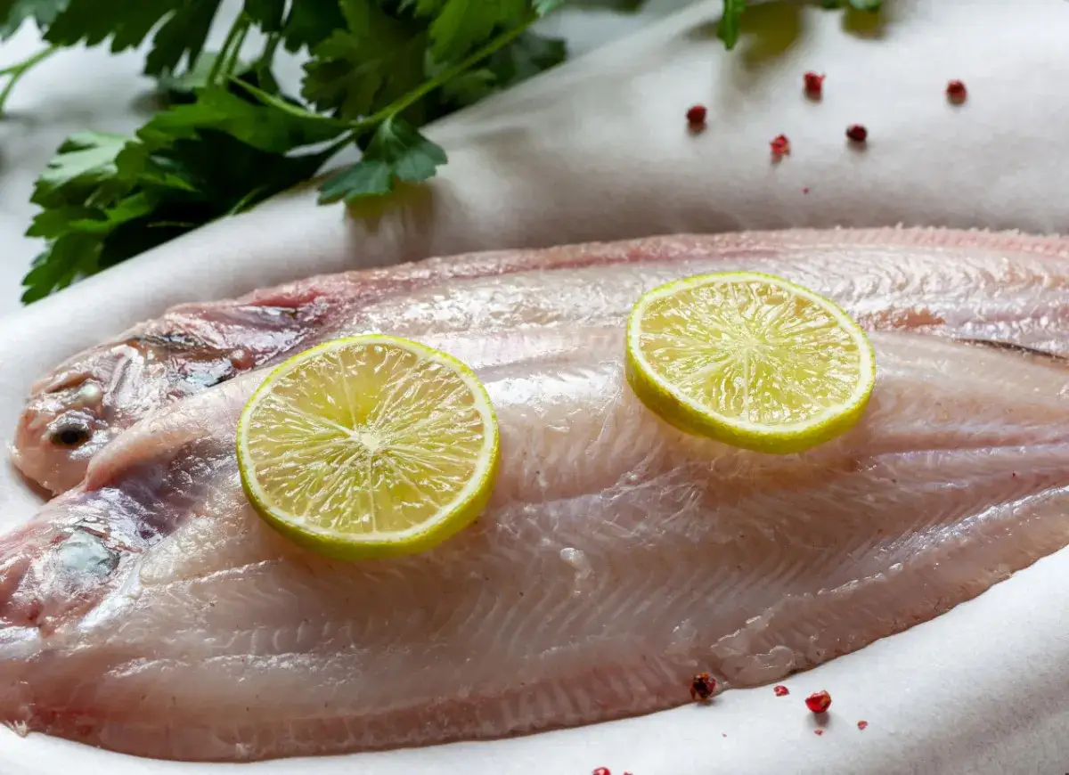Świeża ryba sola z plasterkami limonki i natką pietruszki, gotowa do przygotowania.