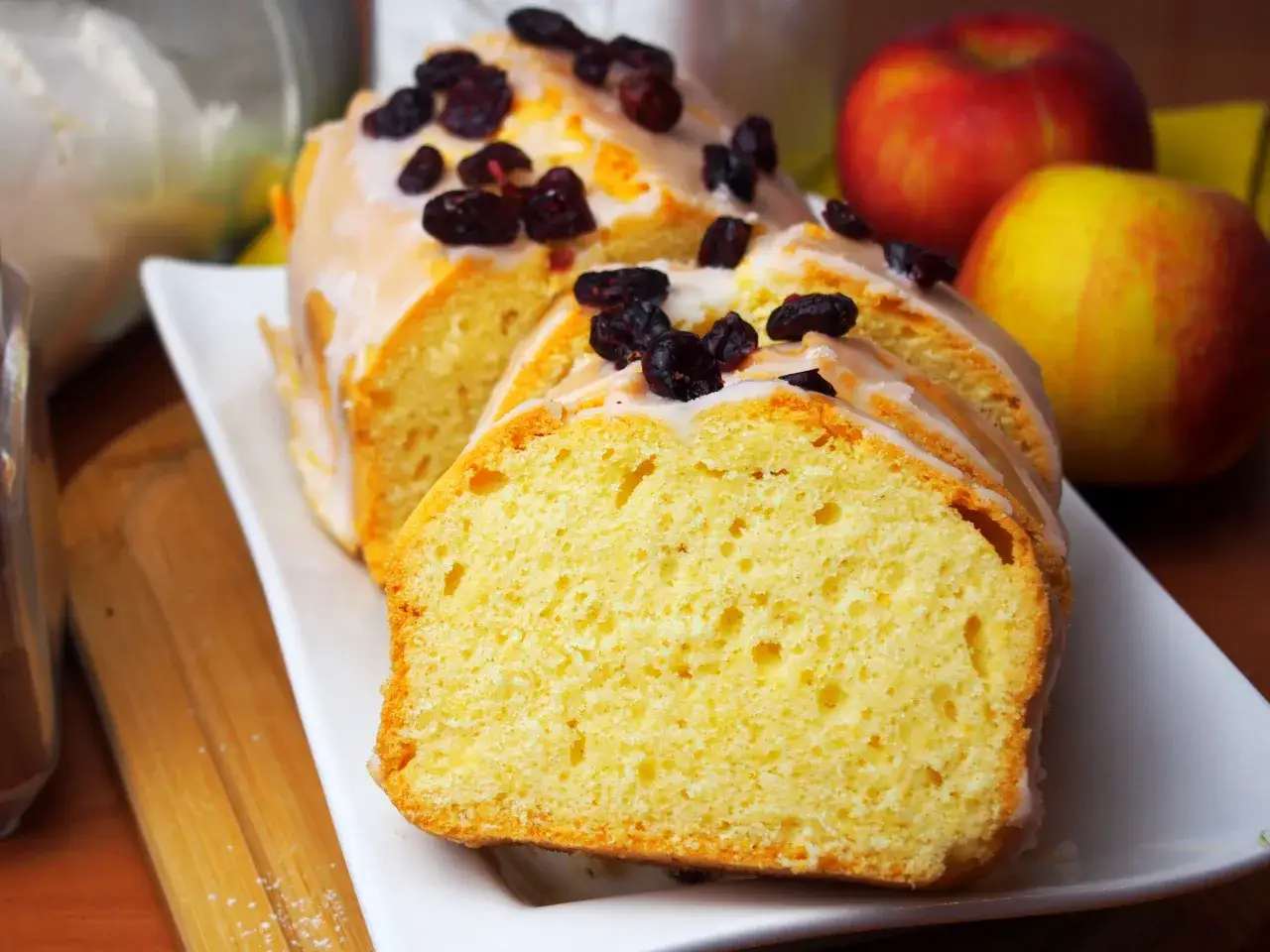 Szybka babka wilgotna, polana lukrem i posypana żurawiną, obok jabłek. Idealna na deser.