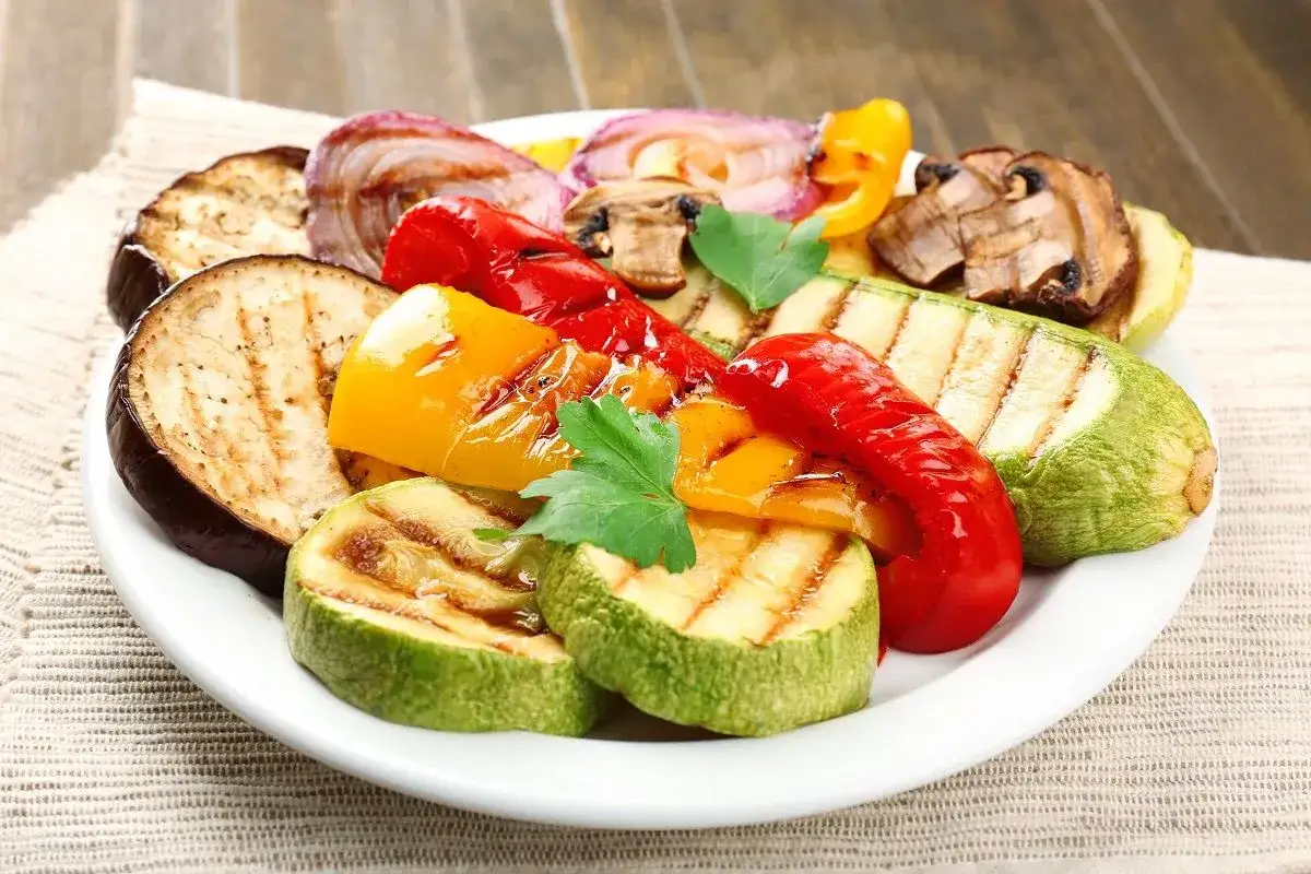 Pyszne warzywa na grilla: grillowany bakłażan, cukinia, papryka, cebula i pieczarki, udekorowane natką pietruszki.